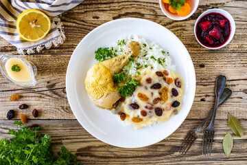 Boiled chicken thigh with white rice and lemon creamy sauce with raisins on wooden table