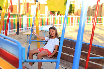 The girl rides on a swing in the playground. Children's outdoor carousels
