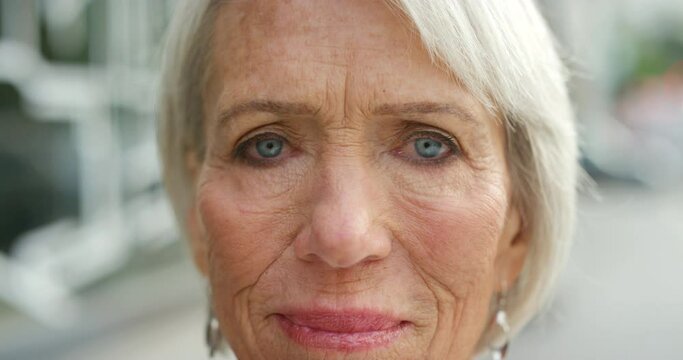 Closeup portrait of a mature woman face against a blurry urban background. Zoom in on a grey haired female senior with wrinkles, looking content while walking in the city on a bright sunny day
