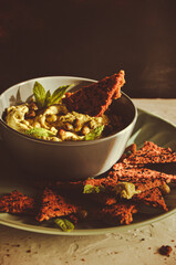 Avocado hummus in bowl with chickpeas, mint leaves and homemade crackers on white background. Healthy raw vegan food