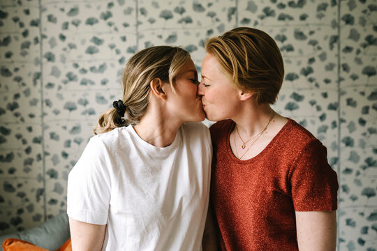 Romantic lesbian couple kissing against wall at home