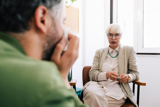 Female psychotherapist discussing with male patient sitting at therapy office