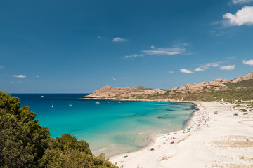 Fototapeta na wymiar Holidaymakers enjoying the sunshine and turquoise Mediterranean sea in the Balagne region of Corsica with the rocky coast of Desert des Agriates behind