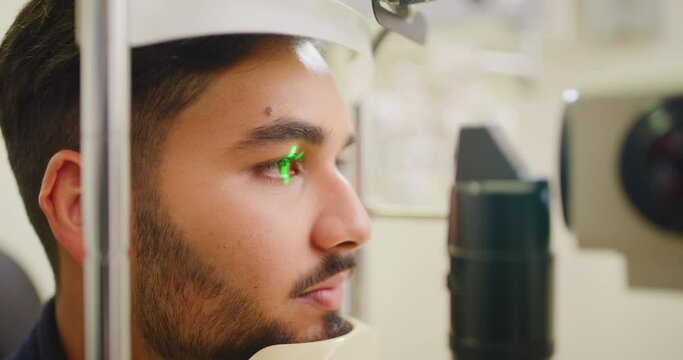 Closeup of a slit lamp machine testing eye and pupil reflexes of a male patient during an optician consult. Headshot of a man at the optometrist, using LED light to examine myopia and retina disease