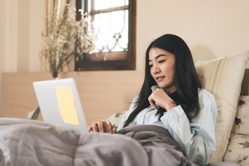 Young adult asian woman using laptop on bed for telemedicine mental health or shopping online