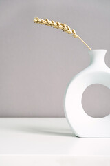 Stylish circle vase with dried spikelets bouquet on light table, copy space. Minimalistic monochrome image. Modern summer still life. 