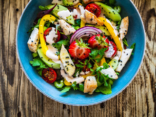 Tasty salad - fried chicken breast, strawberries, mini tomatoes and fresh green vegetables on wooden background
