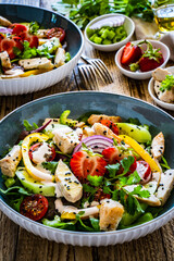 Tasty salad - fried chicken breast, strawberries, mini tomatoes and fresh green vegetables on wooden background
