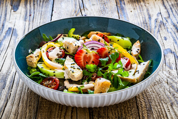 Tasty salad - fried chicken breast, strawberries, mini tomatoes and fresh green vegetables on wooden background
