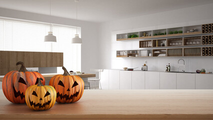 Halloween carved pumpkins on wooden table. Autumn decoration over interior design scene. White and wooden modern kitchen with shelves