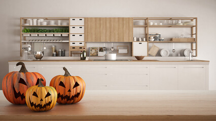 Halloween carved pumpkins on wooden table. Autumn decoration over interior design scene. White modern kitchen with wooden details