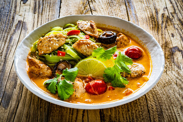 Tom Yum - Thai soup with chicken breast nuggets and rice noodles on wooden table

