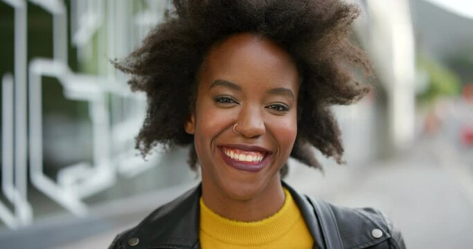 Face of an edgy young woman with afro smiling. Portrait of beautiful trendy black girl laughing, showing her teeth. Confident attractive African American female with positive attitude in the street