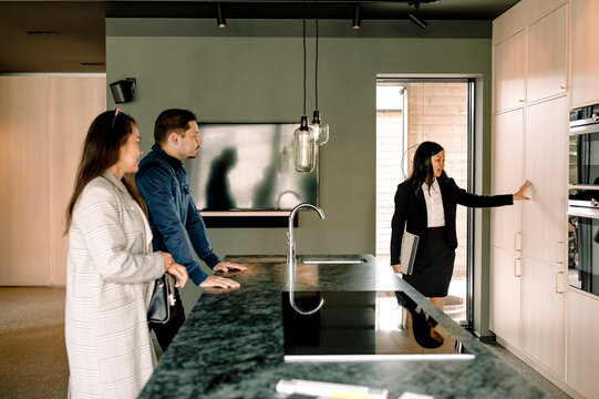 Real estate agent showing kitchen cabinets of new house to couple