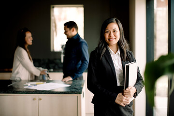 Portrait of smiling real estate agent with couple in background at new home
