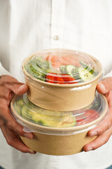 Man in white shirt holding Trendy dish poke bowl - rice, wakame seaweed, tomatoes, cucumber, avocado, salmon in recycled round carton with sustainable fork, takeaway food concept