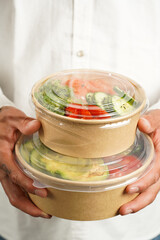 Man in white shirt holding Trendy dish poke bowl - rice, wakame seaweed, tomatoes, cucumber,...