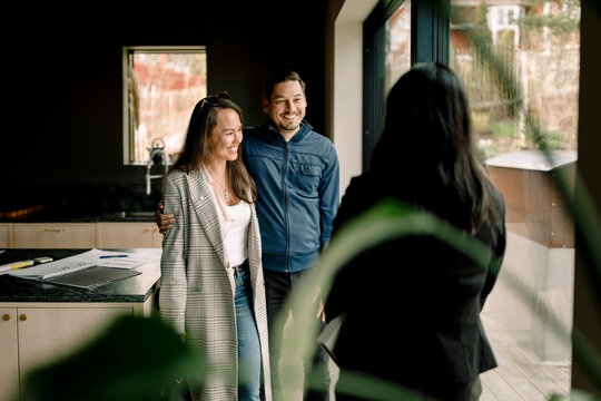 Smiling couple with salesperson standing by window in kitchen
