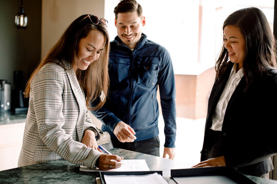 Couple signing contract with realtor at kitchen island of new house - Powered by Adobe