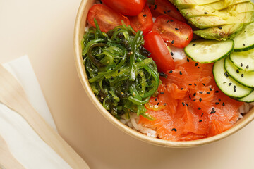 Trendy wholesome dish poke or buddha bowl - rice, wakame seaweed, tomatoes, cucumber, and red fish...