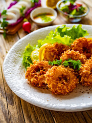 Fried breaded calamari rings with lemon and lettuce on wooden table
