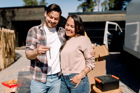Smiling couple looking at key of new house while standing outside new house