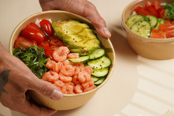 Male hands holding Trendy wholesome dish poke or buddha bowl - rice, wakame seaweed, tomatoes,...