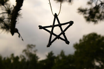 Pentagram hanging from a branches in dark nature. Dark esoteric mystery witchcraft pentagram concept. Dark clouds and forest in background. 