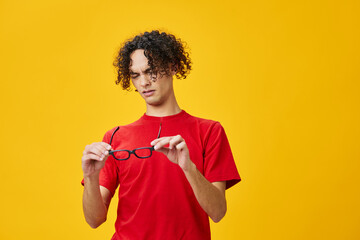 Myopic young student man in red t-shirt looks with disgust at funny eyewear posing isolated on over yellow studio background. The best offer with free place for advertising. Education College concept