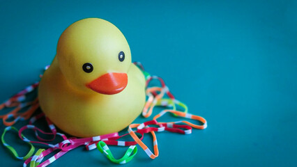 Rubber duck surrounded by colorful rubber bands on blue surface