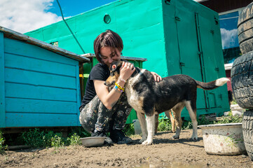Animal shelter volunteer takes care of dogs. Lonely dogs in cage with cheerful woman volunteer.