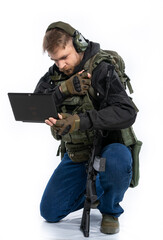 soldier, airsoft player in full gear works on a laptop in combat conditions. a man in headphones, a bulletproof vest, with a backpack and a belt, speaks, transmits information. White background.