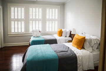 A guest bedroom with two twin beds with turquoise and gray bedspreads and yellow decorative pillows - obrazy, fototapety, plakaty