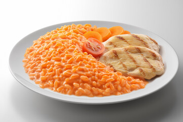 Risotto with red vegetables with grilled chicken in a round white bowl