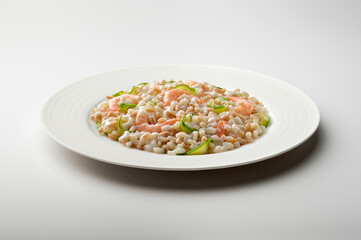 White flat plate of barley spelled rice risotto with shrimps and courgettes