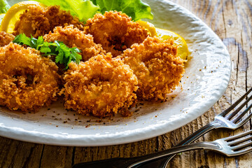 Fried breaded calamari rings with lemon and lettuce on wooden table
