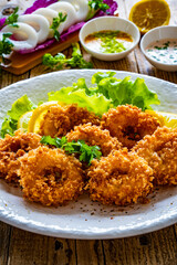 Fried breaded calamari rings with lemon and lettuce on wooden table
