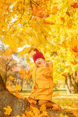 Laughing little child girl plays with maple leaves in the autumn park. Happy child girl having fun...