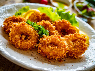 Fried breaded calamari rings with lemon and lettuce on wooden table
