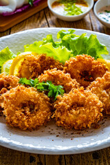 Fried breaded calamari rings with lemon and lettuce on wooden table
