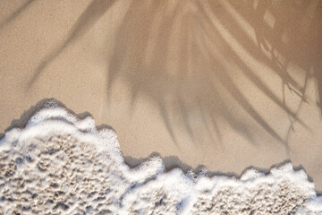 Soft ocean wave on a tropical sandy beach with palm leaves shadow in the summer