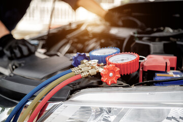 Close up hand of auto mechanic using measuring manifold gauge check the refrigerant and filling car air conditioner for fix and checking for repair service support maintenance and car insurance.