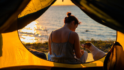 Woman and dog in a tourist tent at sunset. Camping with a pet