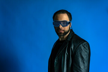 Fototapeta premium portrait of a man in a studio in a black leather coat. model with a beard on a blue background. trendy luminous glasses on the face