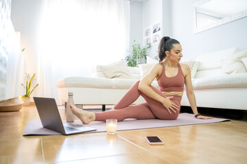 YOUNG GIRL DOING YOGA AND PILATES IN THE LIVING ROOM OF HER HOME WITH THE COMPUTER