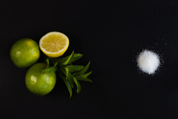 Lemonade recipe on black background: half lemon, two limes, mint leaf, sugar