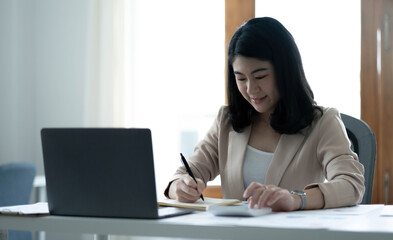 Fototapeta na wymiar Beautiful Asian businesswoman analyzes charts using laptop calculator at the office.