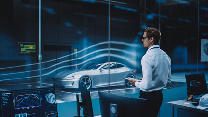 Engineering Research Agency Perform Aerodynamic Testing with a Modern Eco-Friendly Electric Sports Car in a Wind Tunnel. Professional Scientist Works on a Tablet Computer and Changes Testing Options. - obrazy, fototapety, plakaty