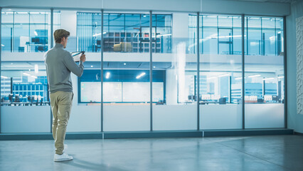 Obraz premium Handsome Stylish Interior Designer Standing in Empty Modern Office and Taking Measurments with an Augmented Reality Software on a Tablet Computer. Business Company Space Under Renovation Process.