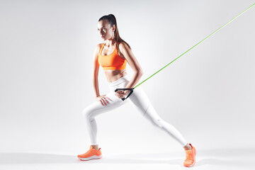 Fototapeta premium Confident woman in sports clothing using resistance band while exercising against white background